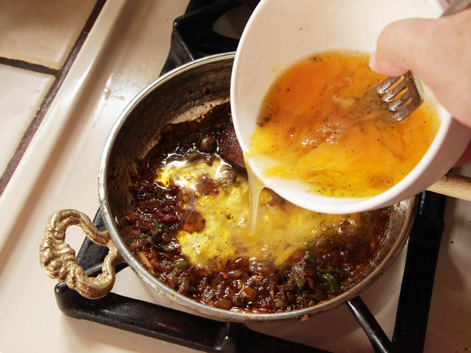 Pouring beaten seasoned eggs into well of cooked peppers, onion, and tomatoes