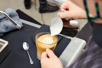 A person pouring milk into an espresso in a glass cup 
