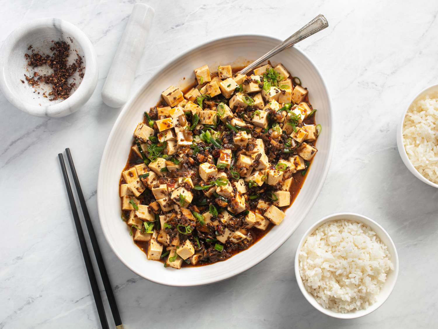 A white oval plate of Vegan Mapo Tofu with bowls of steamed rice on the side