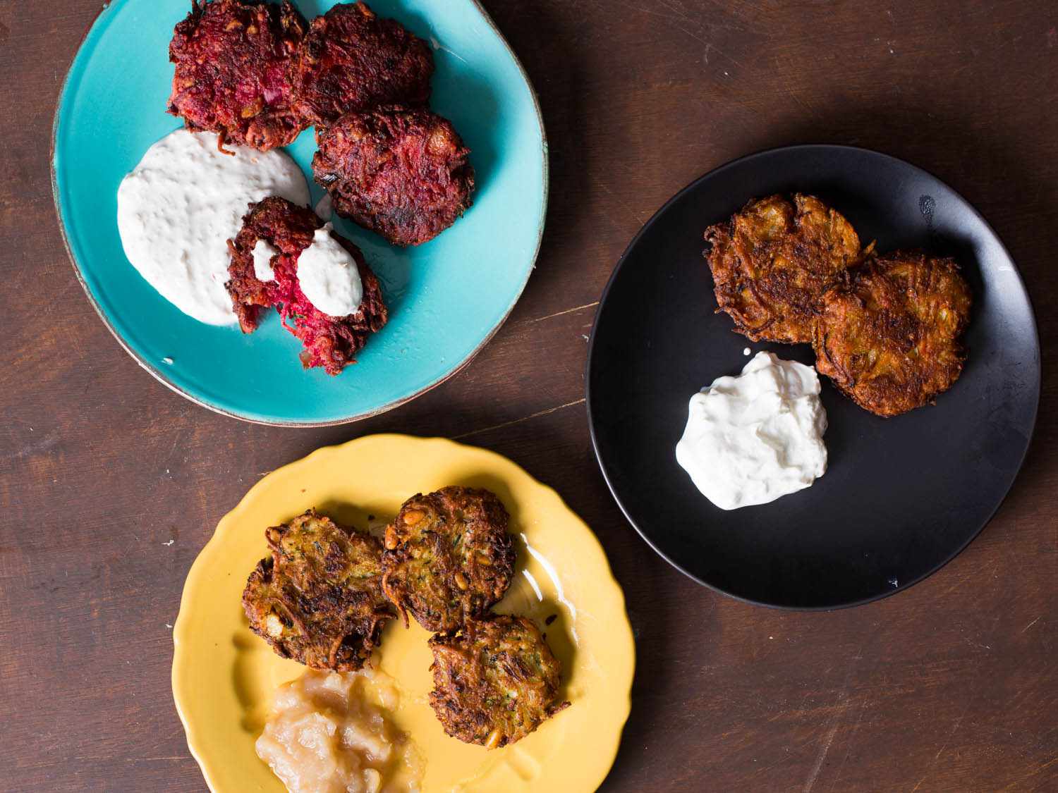 Overhead view of several latke variations: beet-walnut with horseradish cream, spiced sweet potato-carrot-acorn squash, and zucchini-parmesan-pine nut-basil.