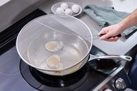 a person placing a splatter screen over eggs frying in a skillet