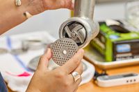 Person placing grinding plate to KitchenAid KSMMGA Metal Food Grinder Attachment