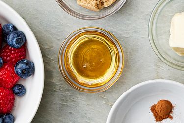 Ingredients for a recipe including honey in a small bowl berries sugar butter and spices arranged on a tabletop