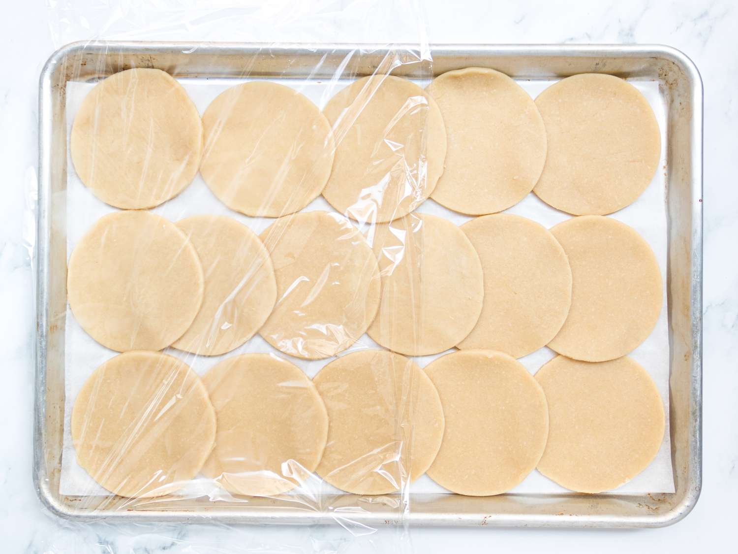 16 dough rounds on a baking sheet, with plastic wrap covering half of the sheet. 