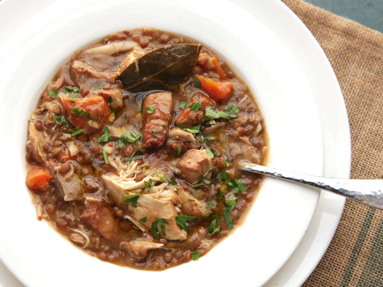 Overhead view of the chicken, lentil, and bacon stew plated in a shallow white soup bowl.
