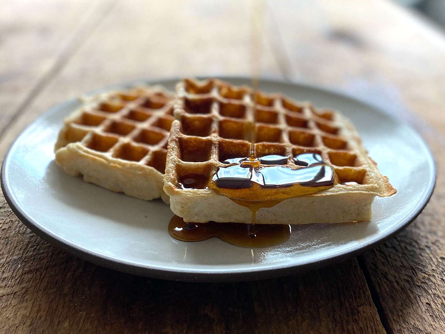 Two sourdough waffles on a plate with maple syrup. 