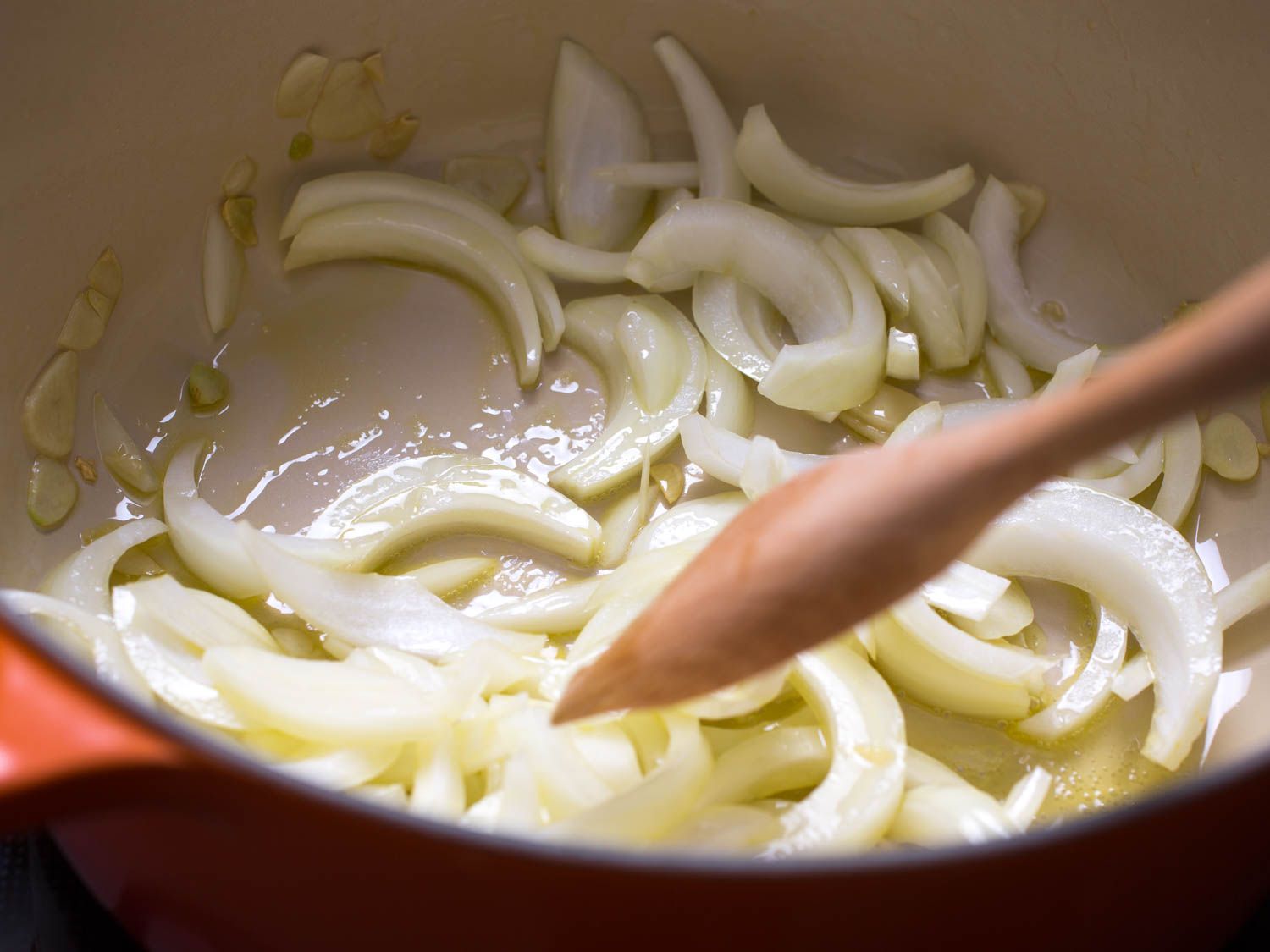 Sliced onions being cooked with garlic and olive oil and stirred with a wooden spoon.