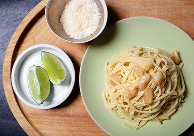 Overhead view of a plate of garlic pasta with grated cheese and lime wedges alongside