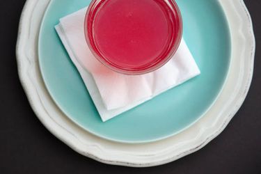 Rhubarb juice in a glass, on a napkin, on a blue plate, on another white plate.