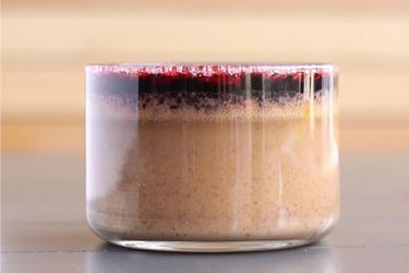 Profile view of a shallow glass of peanut butter pot de crème with red wine syrup.