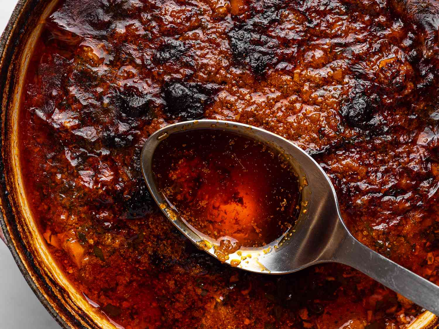 A close-up shot of the surface of the Dutch oven showing a spoon skimming fat off of the surface.