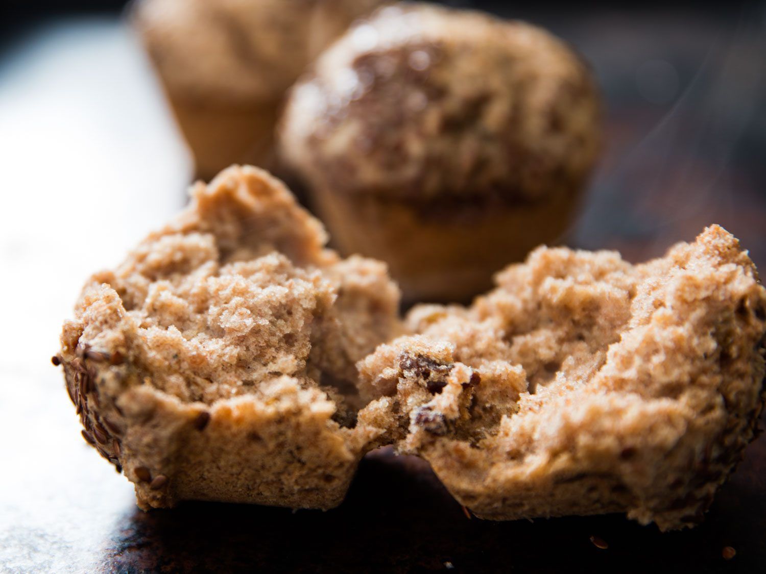 A split-open raisin bran muffin, with two more whole muffins in the background.