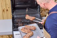 A person using tongs to move steak from the Weber Spirit E-210 Gas Grill to a tray