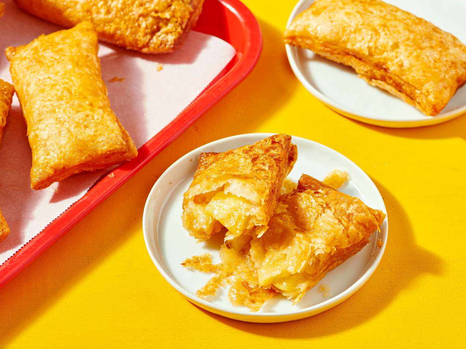 A plate with a cut apple hand pie other pies in a tray and plate nearby