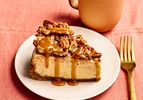 Slice of pecan pie cheesecake on a plate with a fork and mug on a table