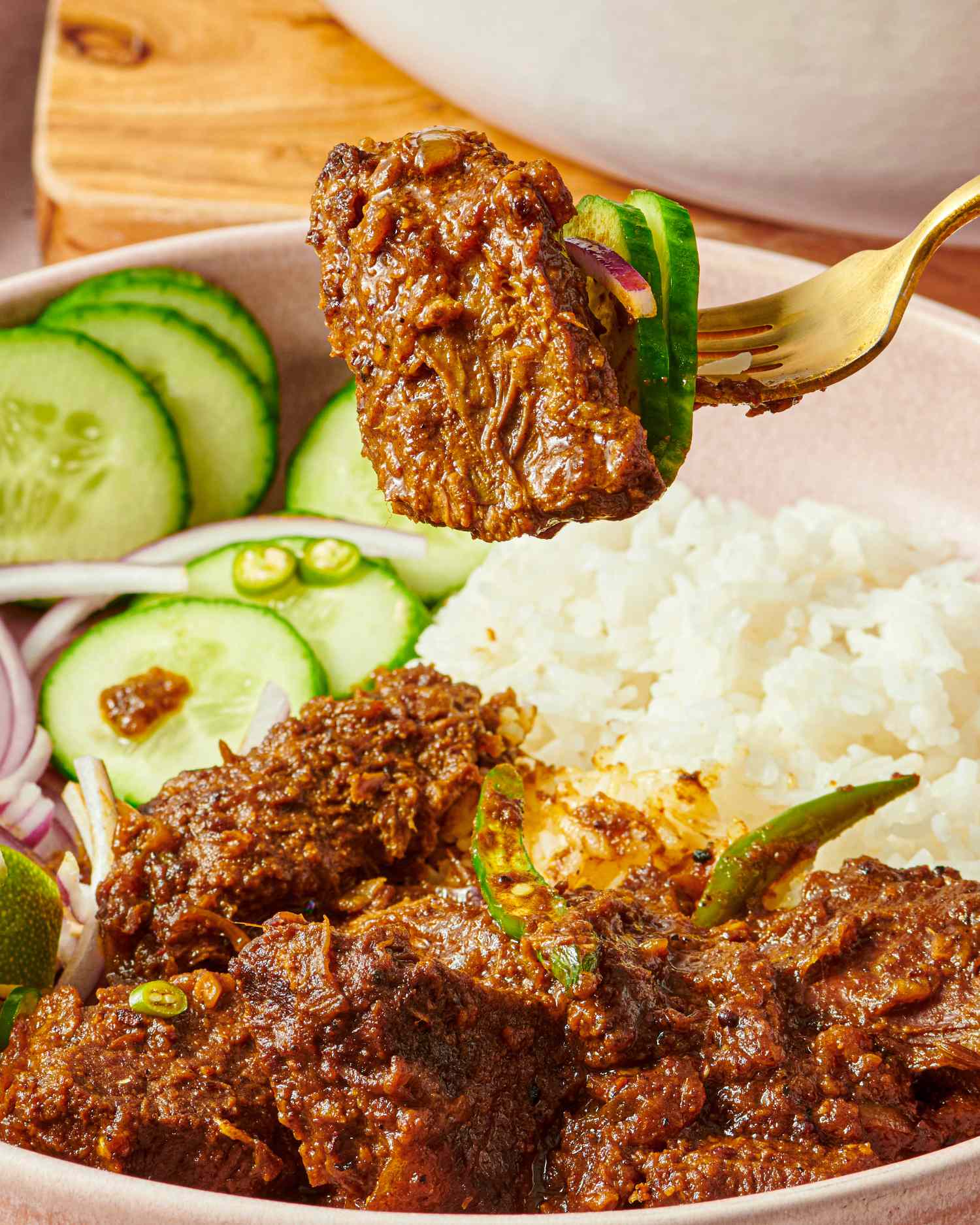 A plate with rice sliced cucumbers and a serving of spiced beef curry