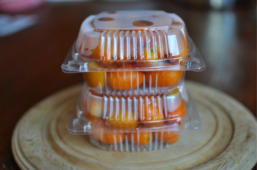 Fresh kumquats in a stack of two clear plastic deli boxes.