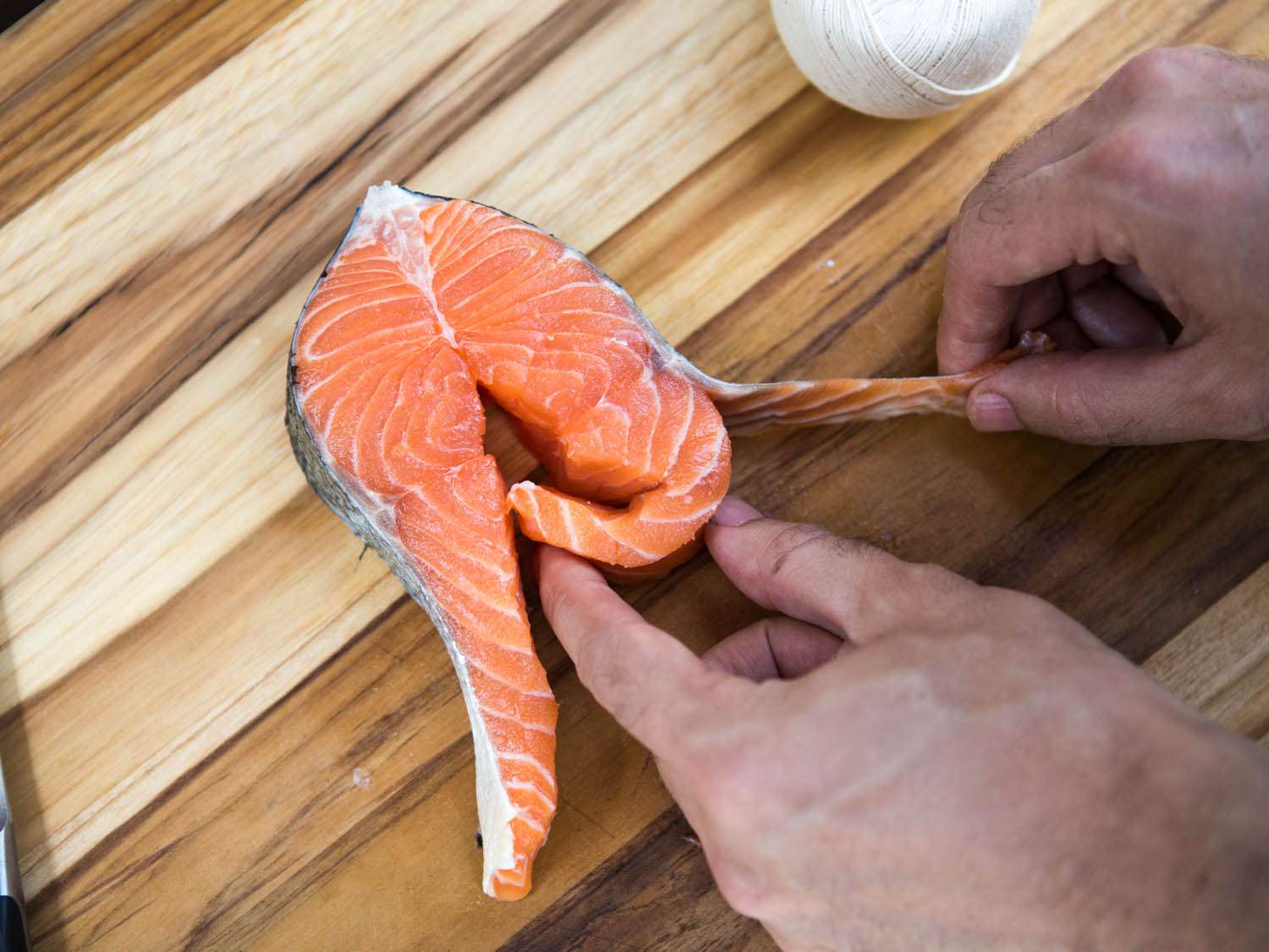 Starting to roll the salmon steak by tucking in one of the belly flaps that has been separated from its skin.