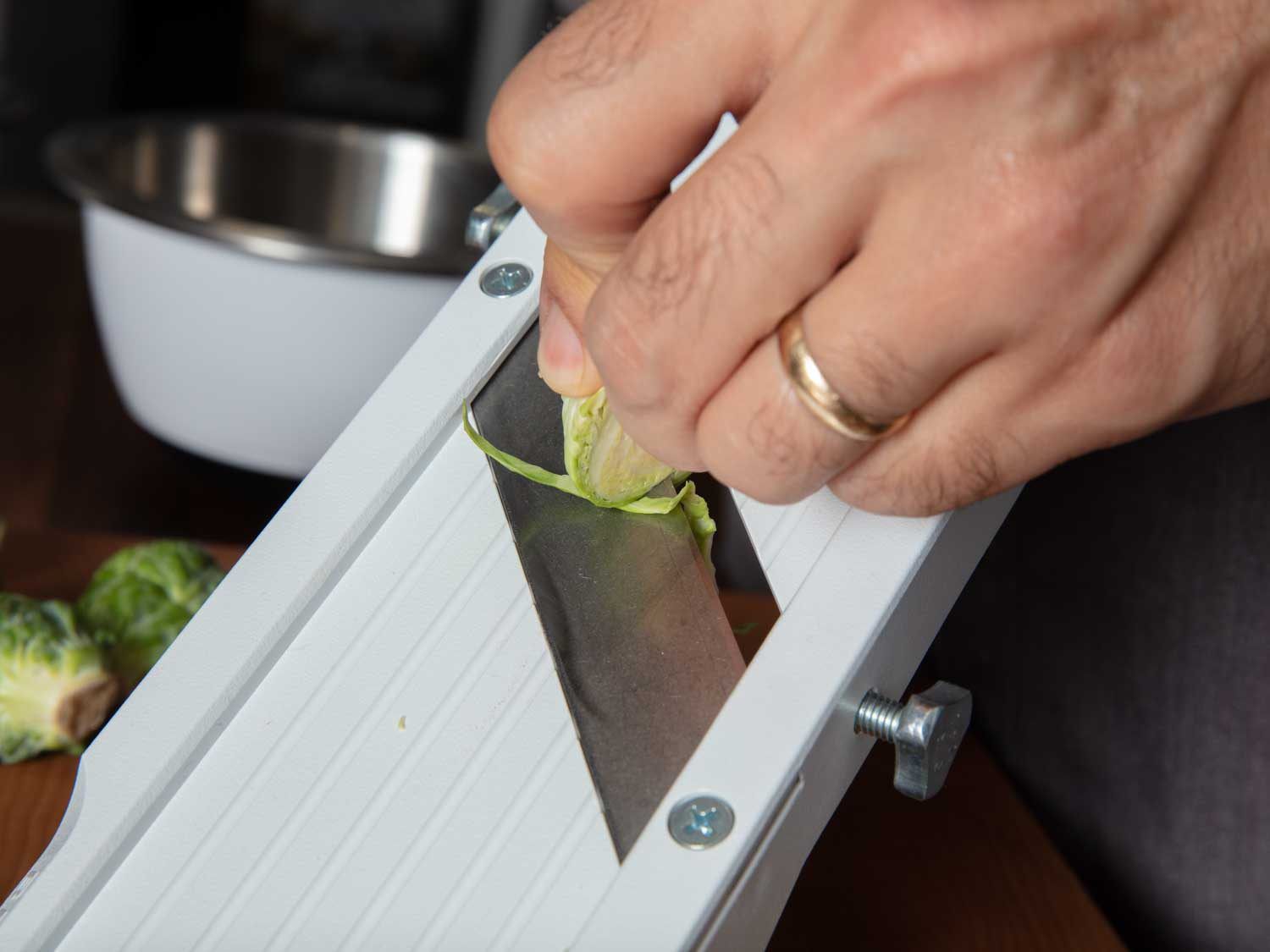 Thinly slicing Brussels sprouts on a mandoline slicer.