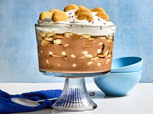 A layered trifle dessert with whipped topping and cookies on top, served in a glass bowl on a stand