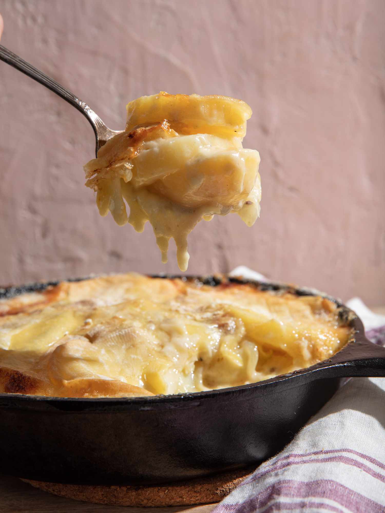 A spoonful of tartiflette is lifted from the pan, cheese dripping down from tender potatoes.