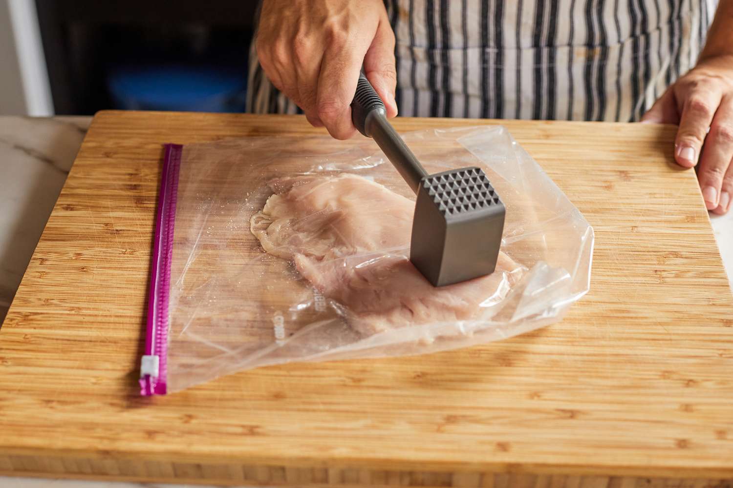 a hand using a meat pounder to flatten a chicken breast inside a zipper lock back