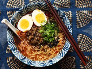 A bowl of ramen topped with a halved hard-boiled egg, smoky eggplant, and scallions.