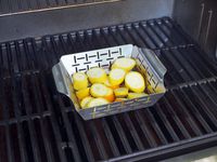 the weber grill basket on a grill with summer squash inside 