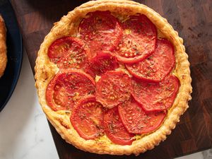 Tomato tart with layered tomato slices on top of a golden crust placed on a wooden surface