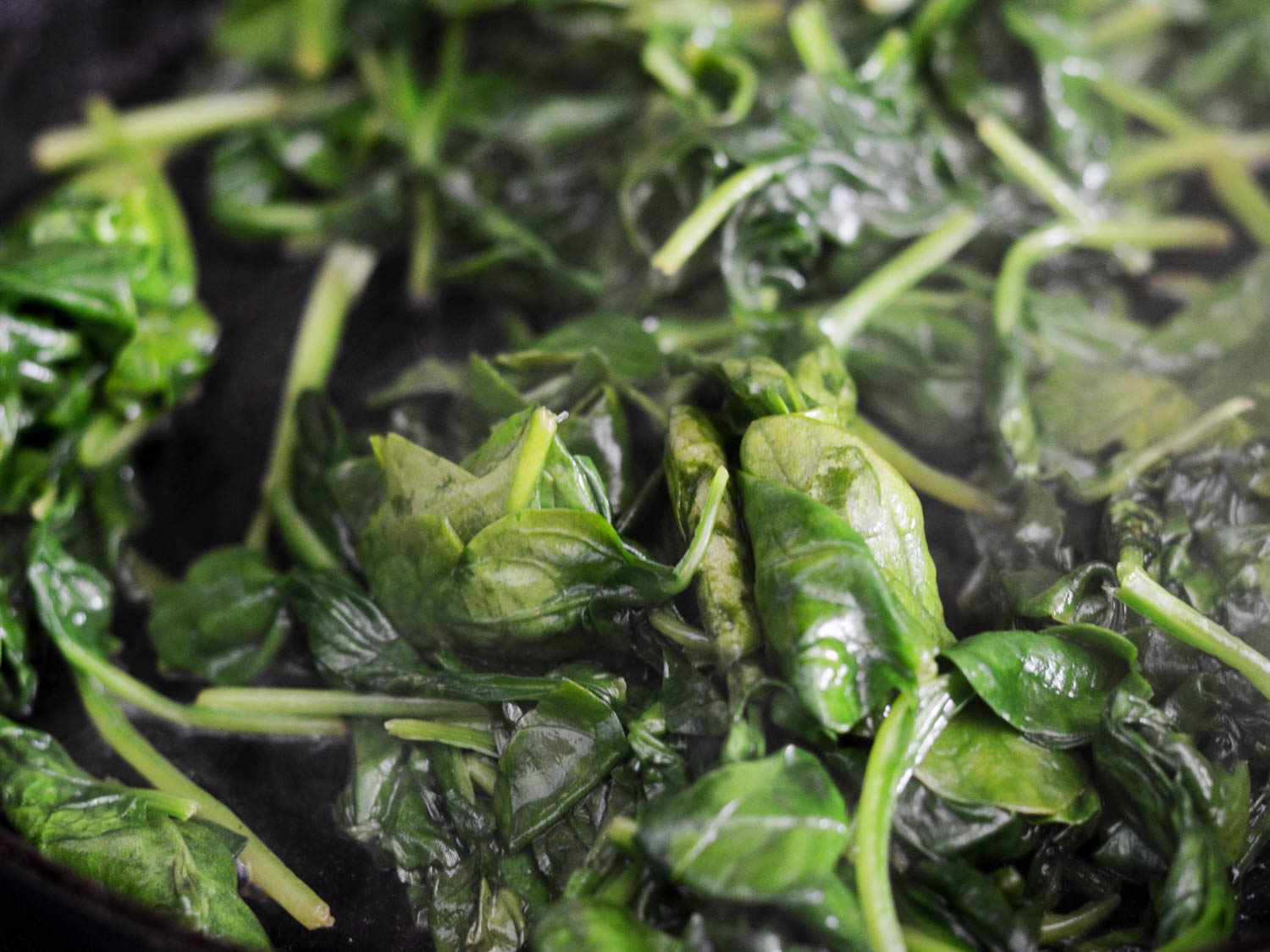 A close-up of cooking, wilting spinach.