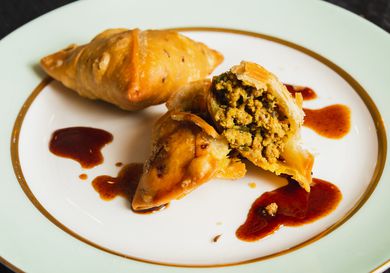 Two kheema samosas on a plate, one broken open to show its interior.