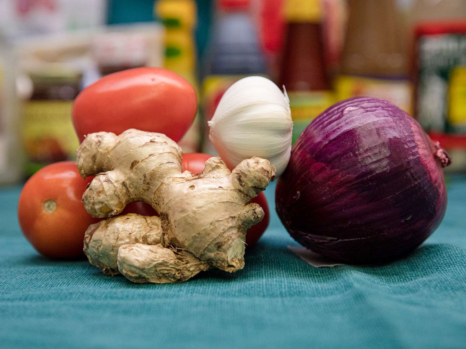 Tomatoes, ginger, garlic, and a red onion on a blue backdrop