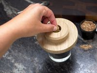a person putting a pinch of wood chips in the cocktail topper