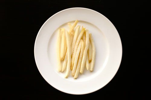 A white porcelain plate on a black background holding a number of frozen McDonald's french fries.