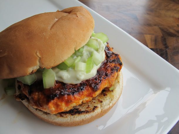 Closeup of a spicy Buffalo chicken burger, shingled slightly on a plate to show the patty and toppings.