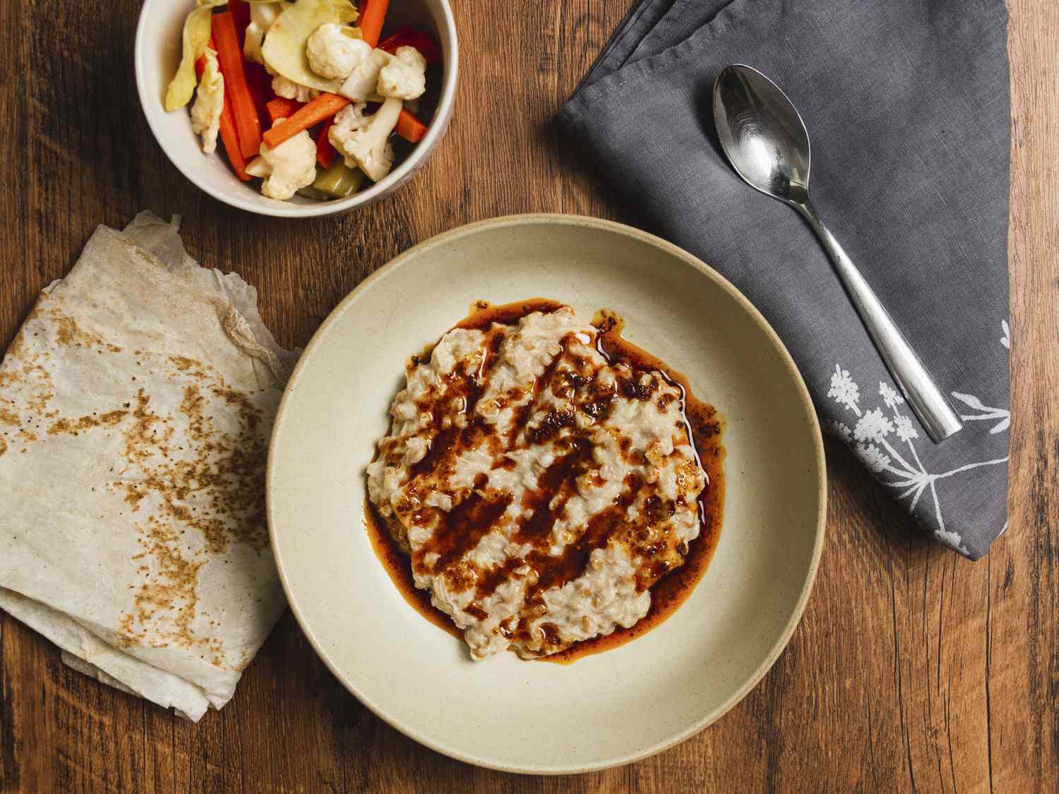 Harissa plated onto a bowl with lavash on the side and a small bowl of vegetables