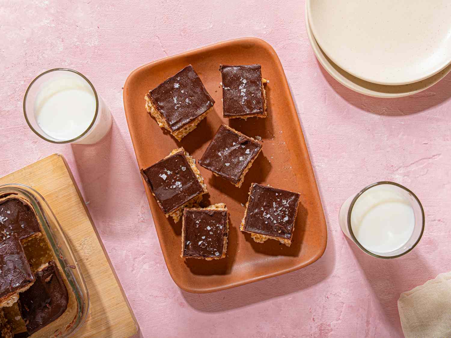Squares of dessert topped with chocolate and accompanied by glasses of milk