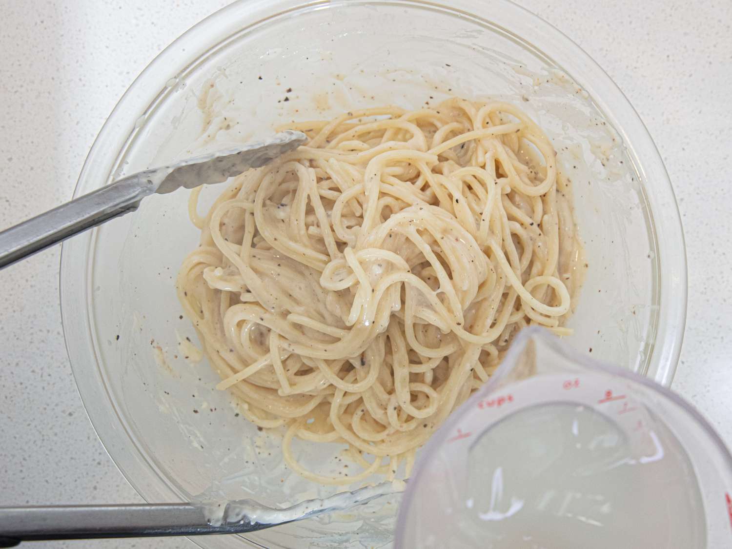 Adding pasta water to spaghetti and cheese paste in a mixing bowl