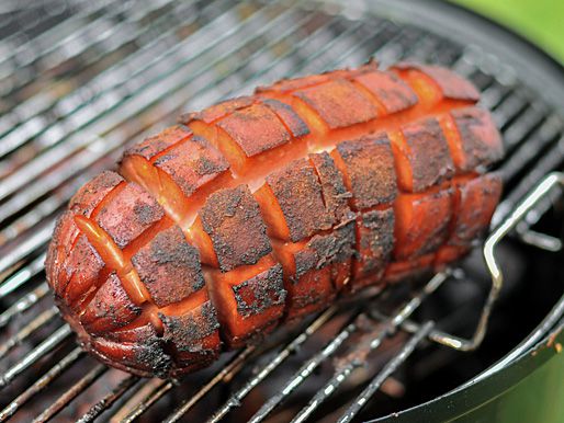 The bologna on a grill grate, fully smoked and crispy on the outside. The sausage has expanded and the incisions have opened wide.