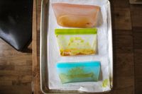 Three reusable food storage bags with remnants of food placed on a tray with a paper towel underneath
