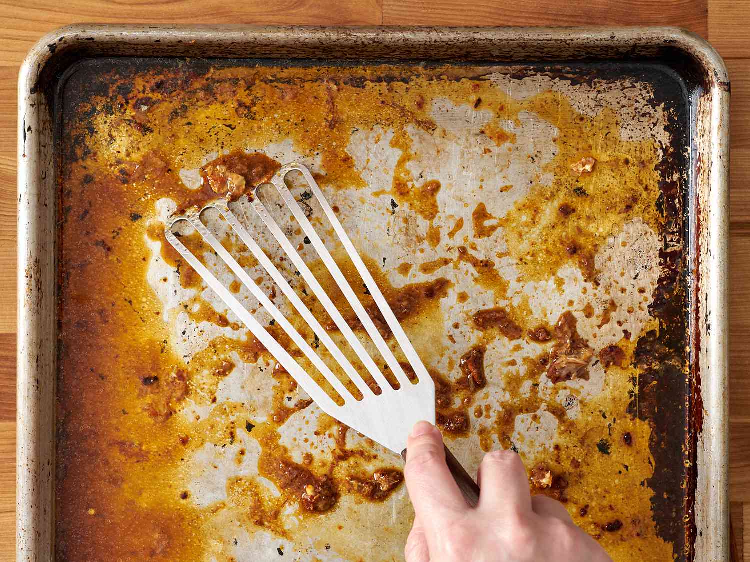 Slotted spatula scraps up chicken fat from a baking sheet.
