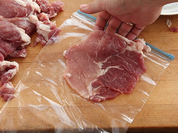 A hand lifting up a thin piece of pounded pork sirloin from sheet of plastic