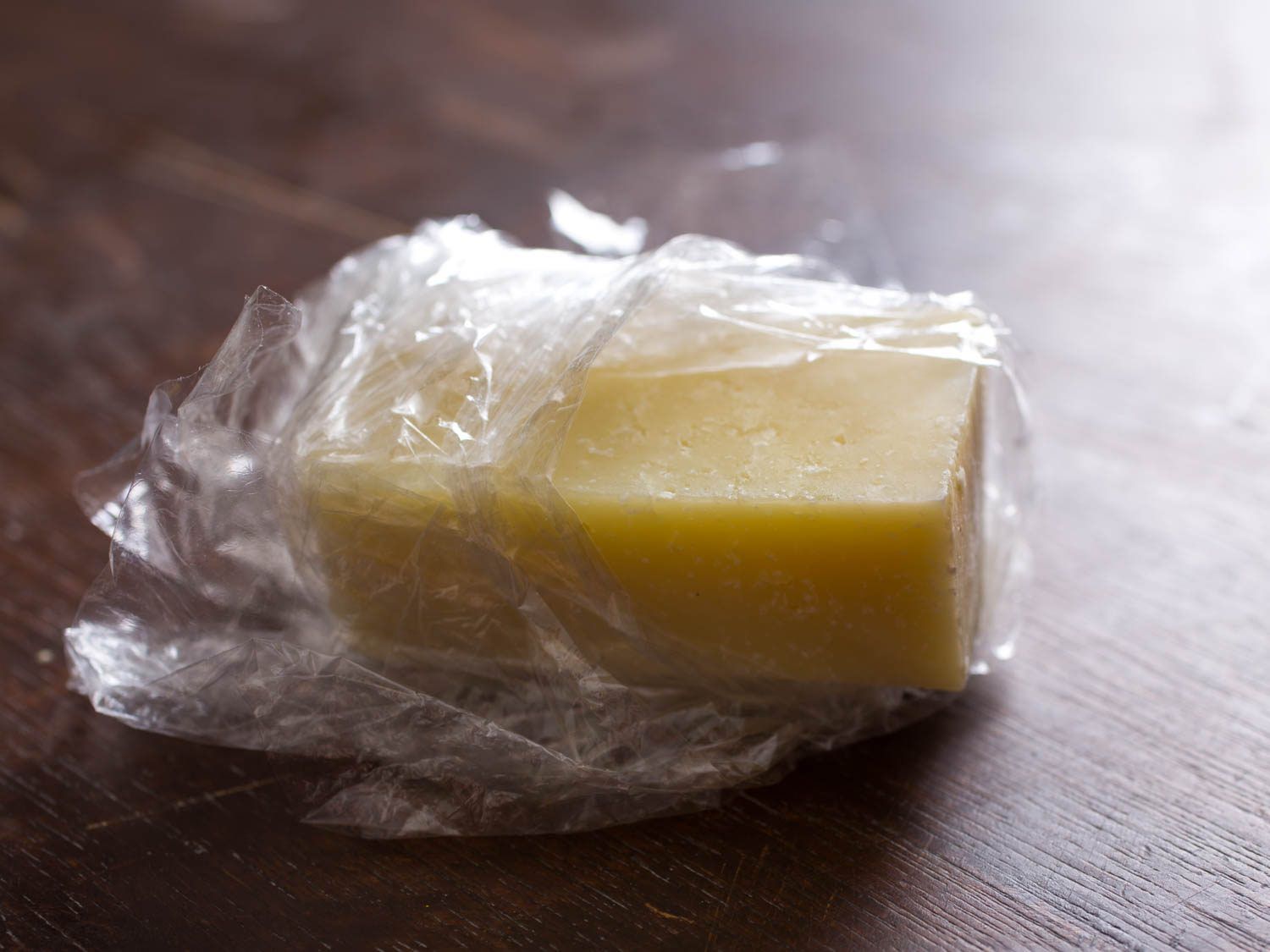 A hunk of cheese partially wrapped in plastic