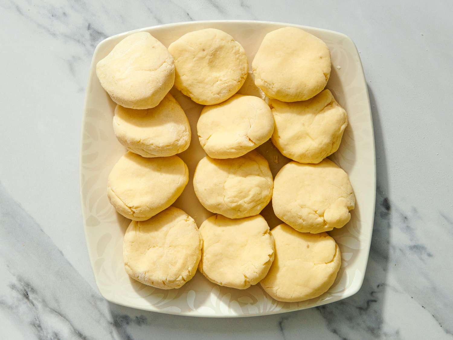 A plate of lefse dough pieces prepared for cooking arranged neatly on a white plate