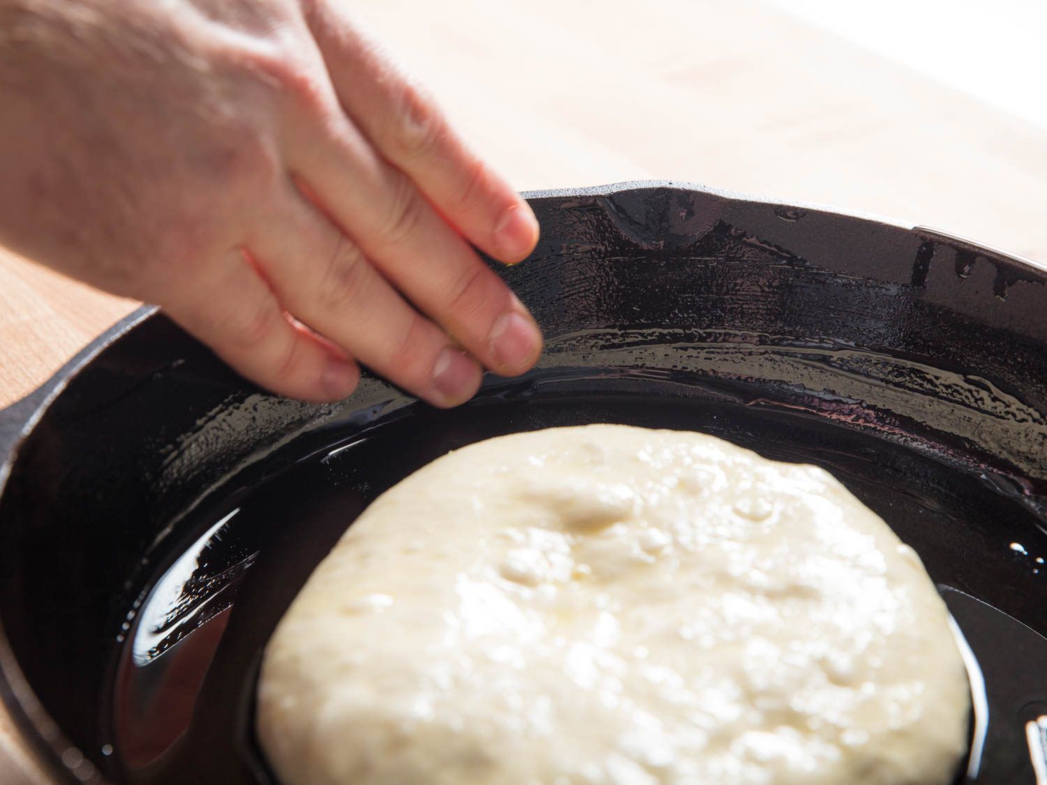 Pan pizza dough placed in greased cast iron pan to proof.