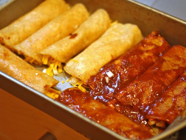 A pan filled half with filled corn tortilla rolls dipped in red chile gravy and half without.