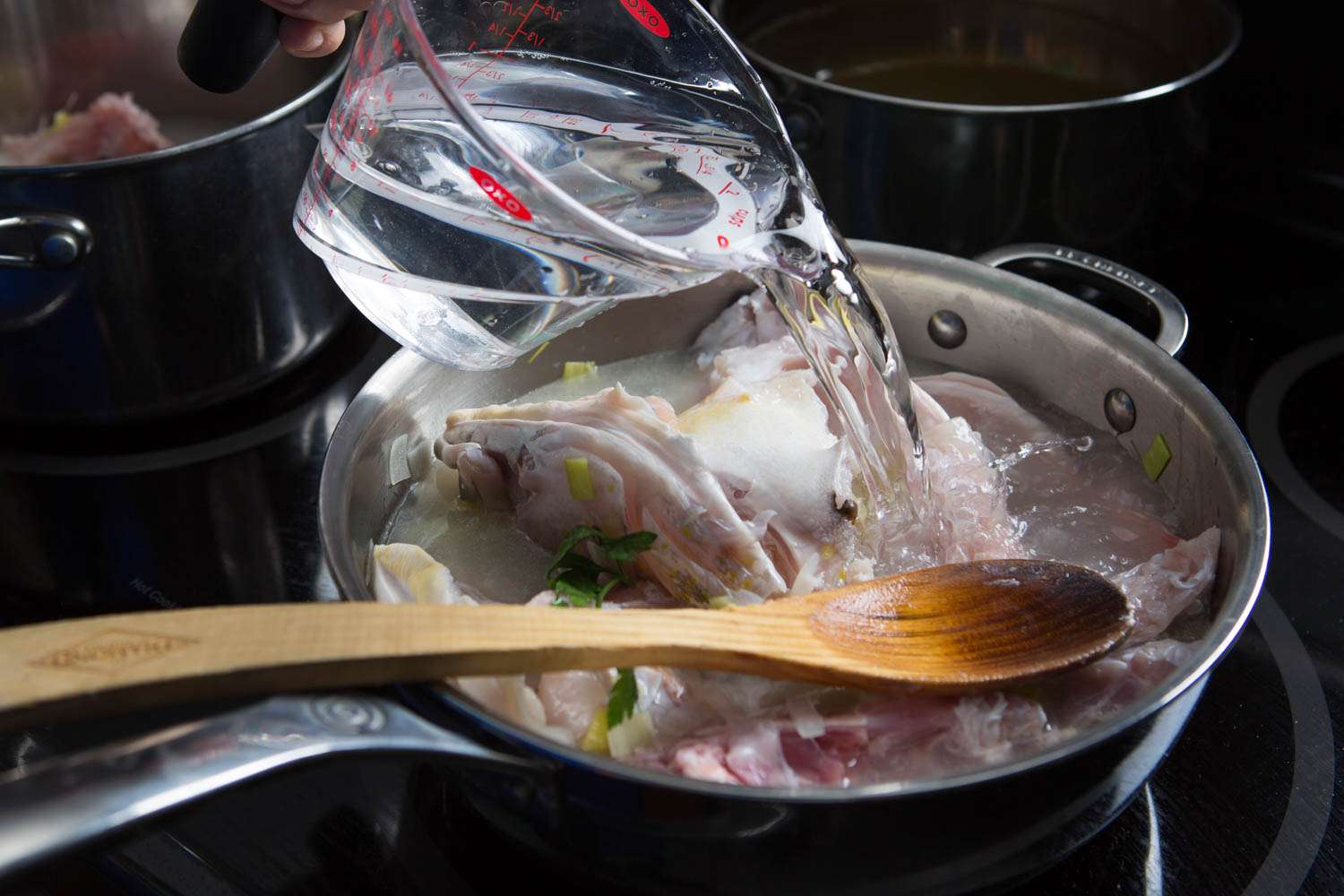 Adding water to a pot of fumet. 