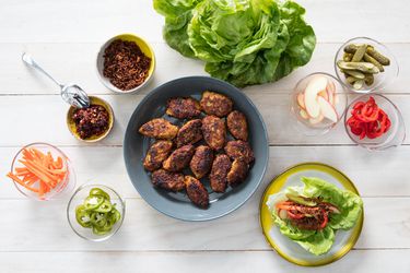 Overhead view of Vietnamese-style chicken meatballs, served on a platter with butter lettuce leaves, pickles, sliced chiles, and assorted condiments.