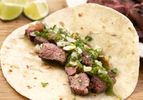 Sliced marinated grilled flank steak nestled in a flour tortilla with topped with green salsa 