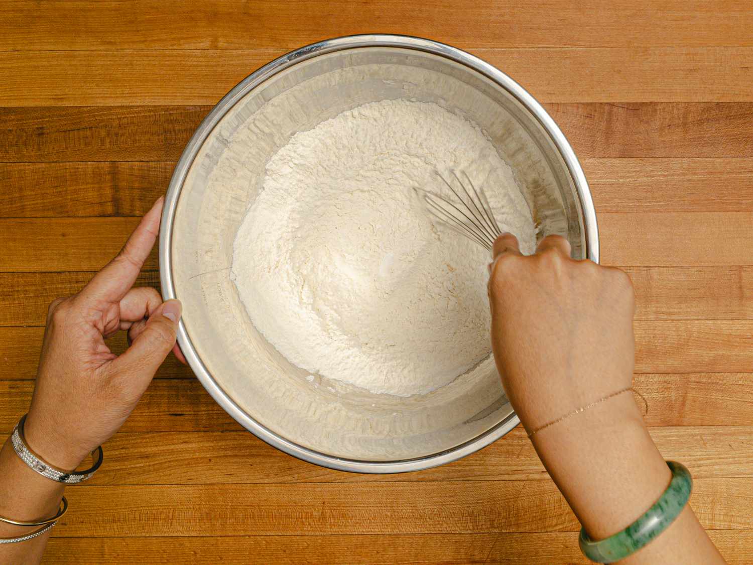Hands whisking dry ingredients in a metal mixing bowl